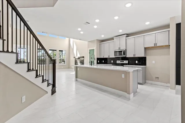 a kitchen with stainless steel appliances kitchen island granite countertop a refrigerator a stove a sink and white cabinets with wooden floor