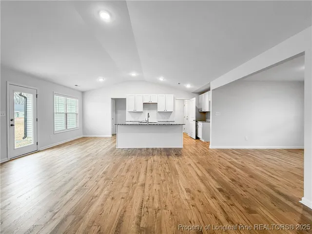a view of empty room with wooden floor and kitchen