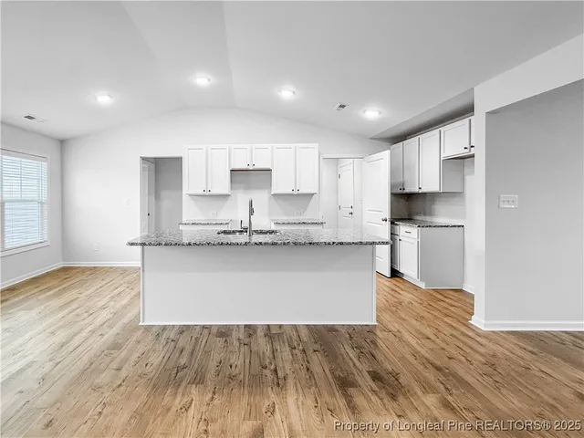 a large kitchen with kitchen island a sink dishwasher a refrigerator and white cabinets with wooden floor