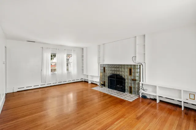a view of an empty room with wooden floor fireplace and a window
