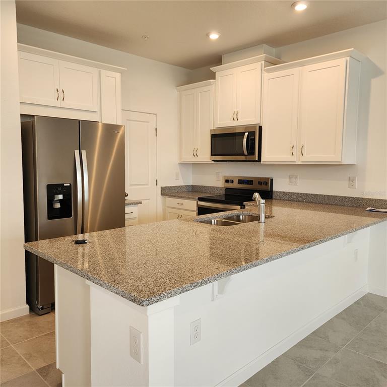 4232 Sadler Road Apopka, FL 32712 - Photo 6 of 31 a kitchen with stainless steel appliances granite countertop a refrigerator a stove a sink a microwave and white cabinets