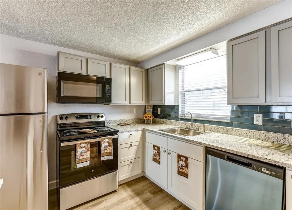 9911 Aquarius Drive, Unit 8 Port Richey, FL 34668 - Photo 5 of 25 a kitchen with stainless steel appliances granite countertop a stove sink microwave and refrigerator