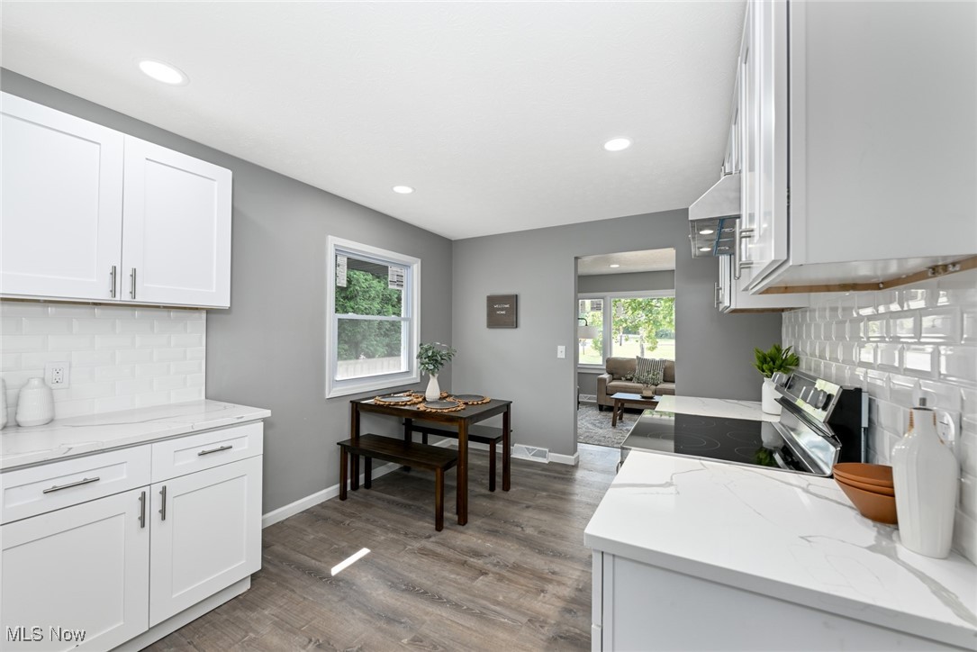 263 Forbes Road Bedford, OH 44146 - Photo 10 of 20 Kitchen featuring light stone countertops, backsplash, stainless steel range with electric stovetop, wood-type flooring, and white cabinetry