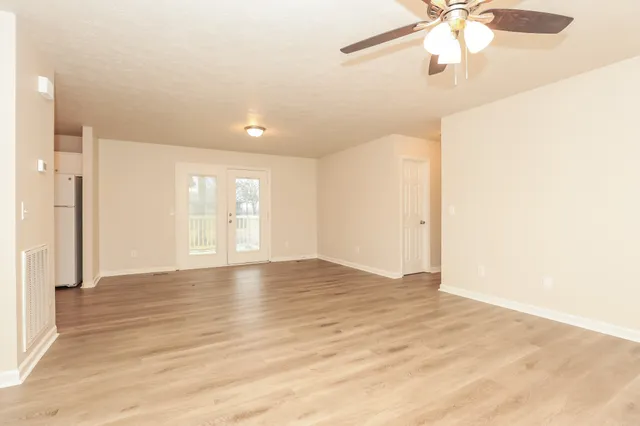 an empty room with wooden floor fan and windows