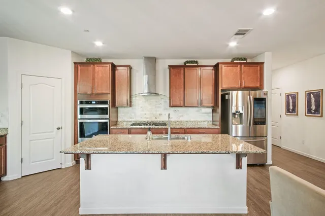 a kitchen with stainless steel appliances granite countertop a refrigerator a stove and a sink with wooden floor
