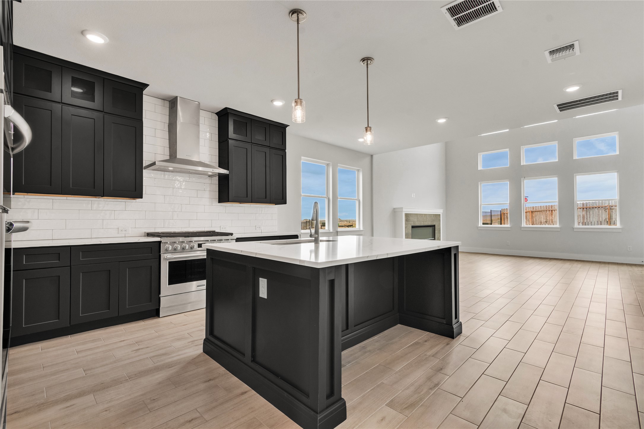 8500 Red Bottle Brush Road Lago Vista, TX 78645 - Photo 7 of 33 A contemporary kitchen features an inviting island with a sink and pendant lighting, opening to a living area with a fireplace and tall windows.