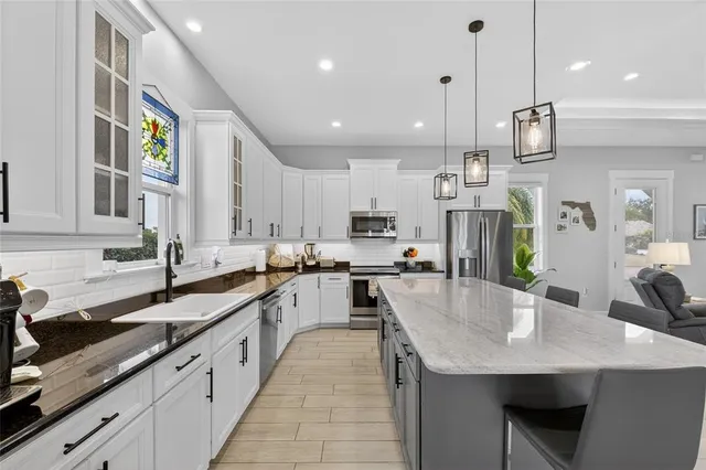 a open kitchen with stainless steel appliances granite countertop a kitchen island a stove a refrigerator a sink a dining table and chairs with wooden floor