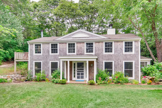 front view of a brick house with a yard and large trees