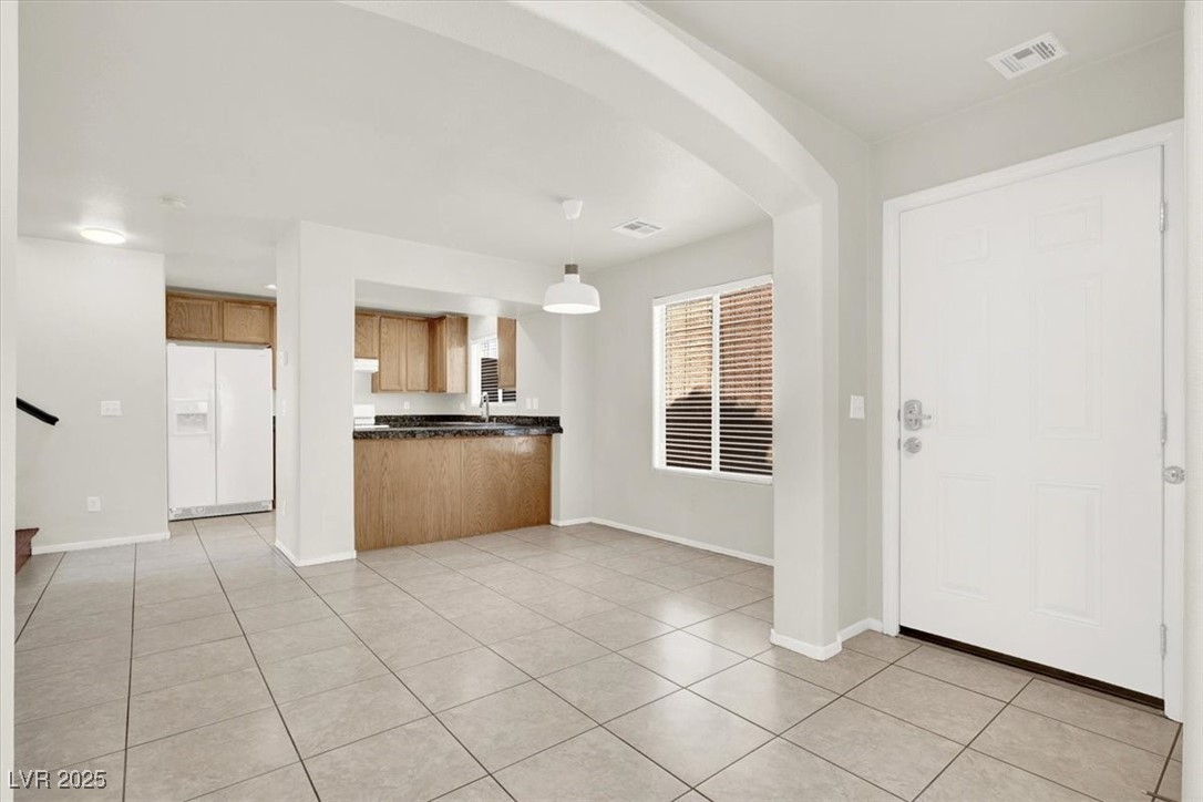 6909 Graceful Cloud Avenue Las Vegas, NV 89122 - Photo 5 of 33 Kitchen featuring dark countertops, arched walkways, pendant lighting, white fridge with ice dispenser, and light tile patterned floors