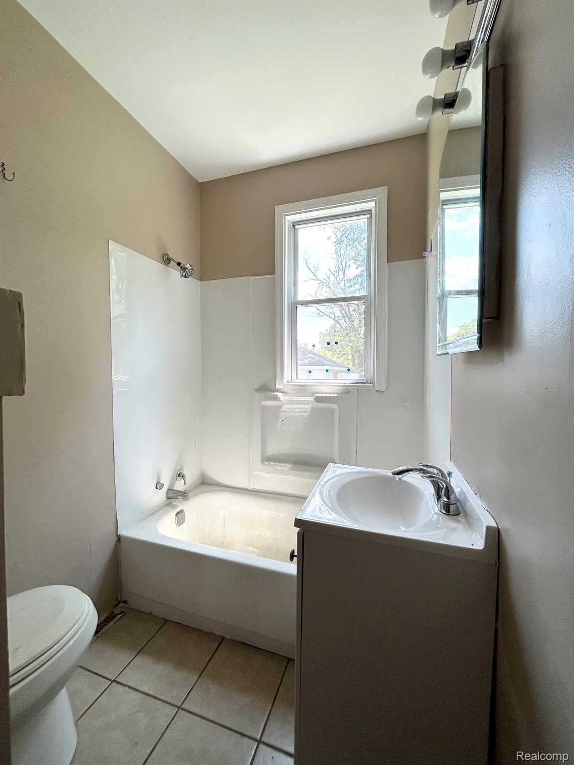 2414 Thom Street Flint, MI 48506 - Photo 8 of 8 Bathroom featuring a single-pane window, white vanity with integrated sink, chrome faucet, wall-mounted mirror with vanity lighting, and a white bathtub with a shower fixture