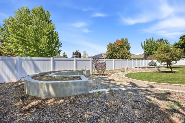 776 Flint Street Layton, UT 84041 - Photo 28 of 41 Expansive backyard featuring a white vinyl privacy fence, concrete raised garden beds, a gravel path, mature trees, and a lawn area