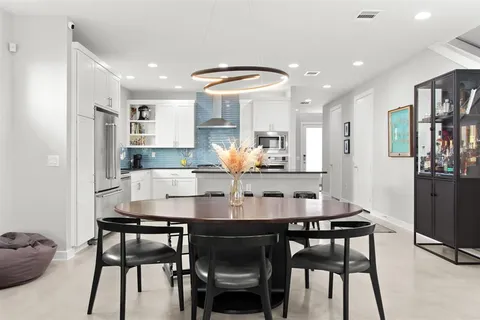 a kitchen with stainless steel appliances kitchen island granite countertop a dining table chairs and a refrigerator