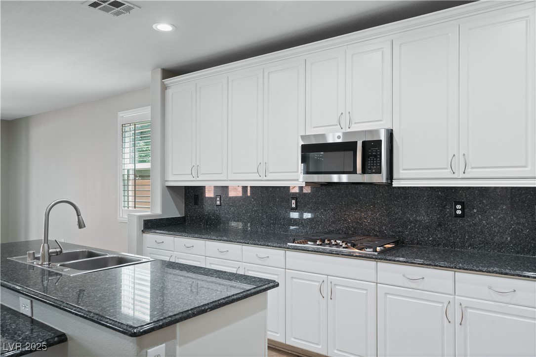 312 Pocono Ranch Avenue North Las Vegas, NV 89031 - Photo 7 of 34 Kitchen with decorative backsplash, white cabinets, a sink, appliances with stainless steel finishes, and visible vents