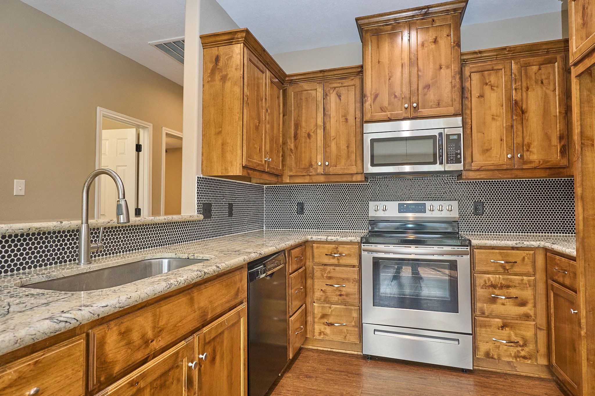 1807 Nuches Lane Bryan, TX 77803 - Photo 11 of 27 This kitchen features warm wood cabinetry, stainless steel appliances, and a sleek tile backsplash. The granite countertops and hardwood flooring create a cozy and inviting atmosphere.