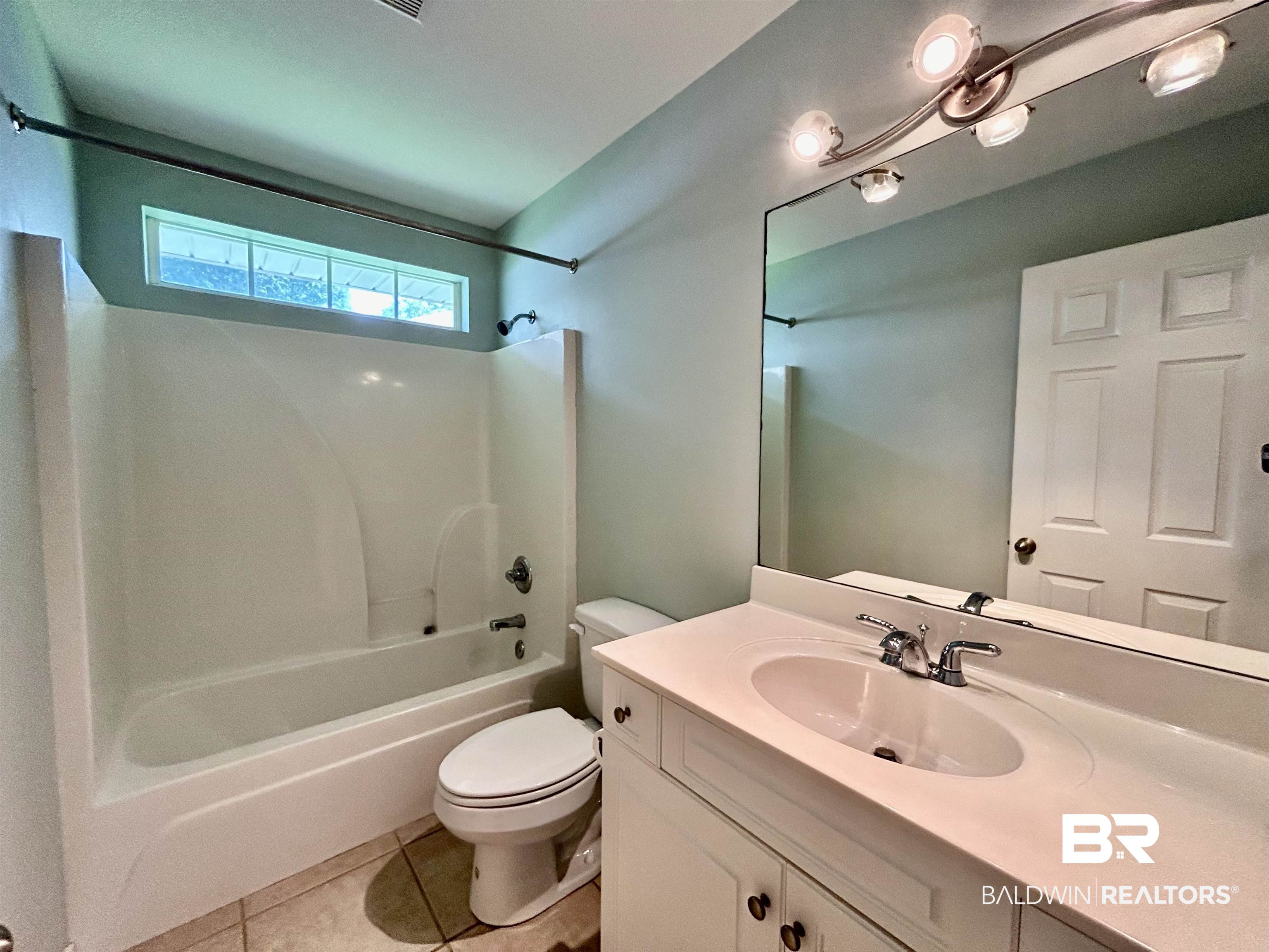 7198 Raintree Lane Gulf Shores, AL 36542 - Photo 22 of 33 Bathroom featuring a white bathtub and shower combination, an integrated sink vanity with a large mirror, a toilet, and neutral-toned floor tiling