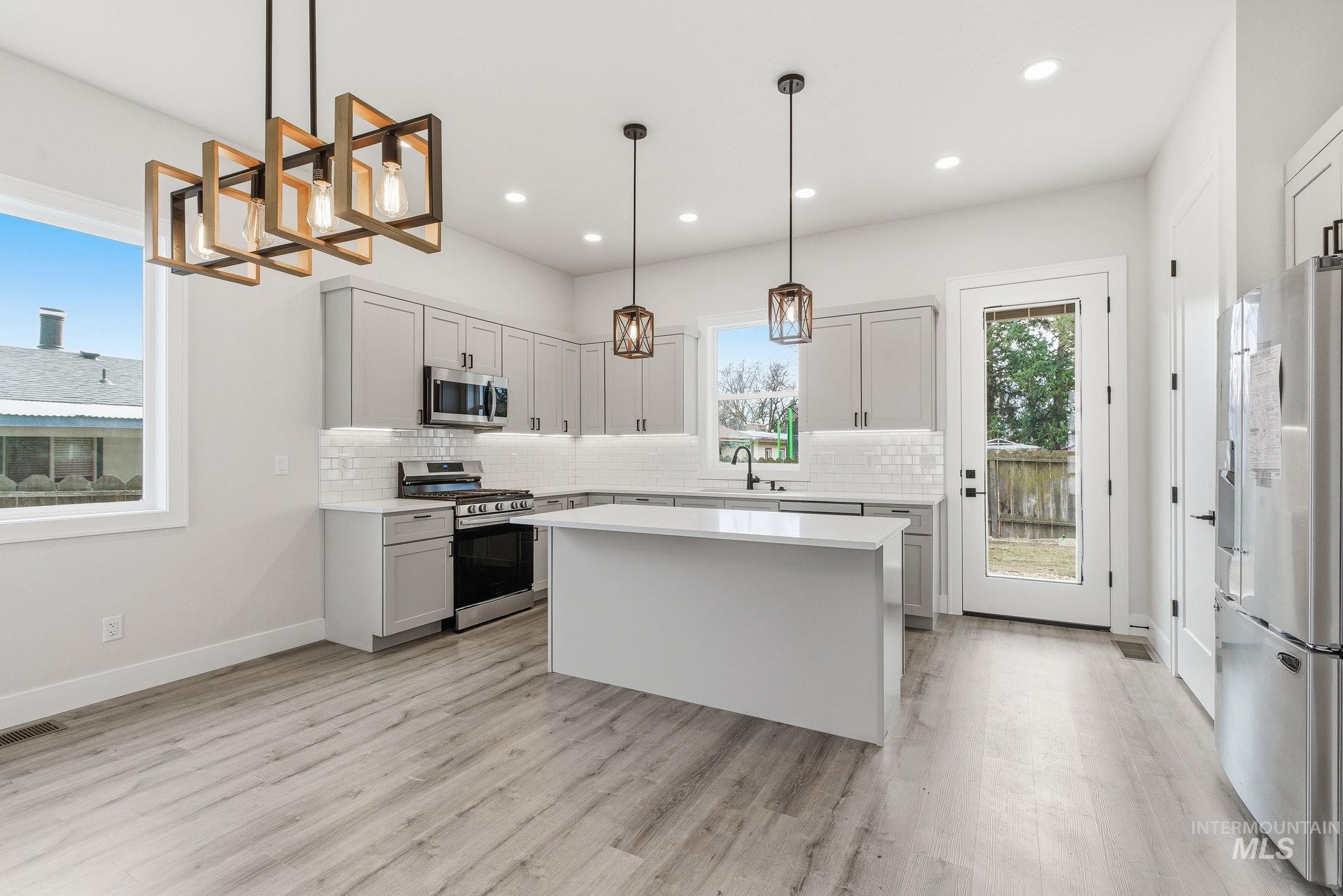 6821 West Ustick Road Boise, ID 83704 - Photo 11 of 42 Kitchen with tasteful backsplash, stainless steel appliances, a kitchen island, a chandelier, and light wood-style floors