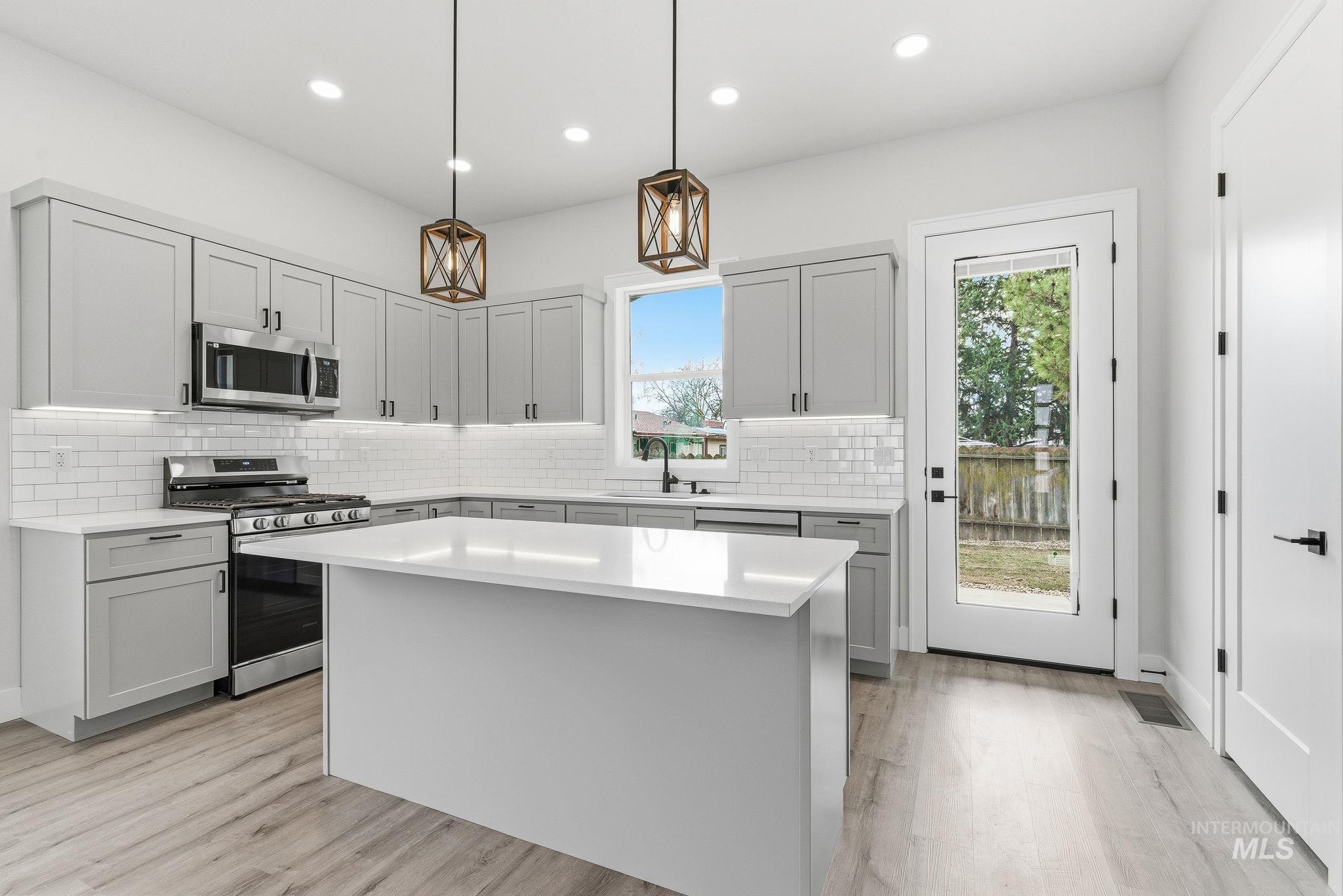 6821 West Ustick Road Boise, ID 83704 - Photo 12 of 42 Kitchen with decorative light fixtures, stainless steel appliances, a kitchen island, gray cabinetry, and decorative backsplash