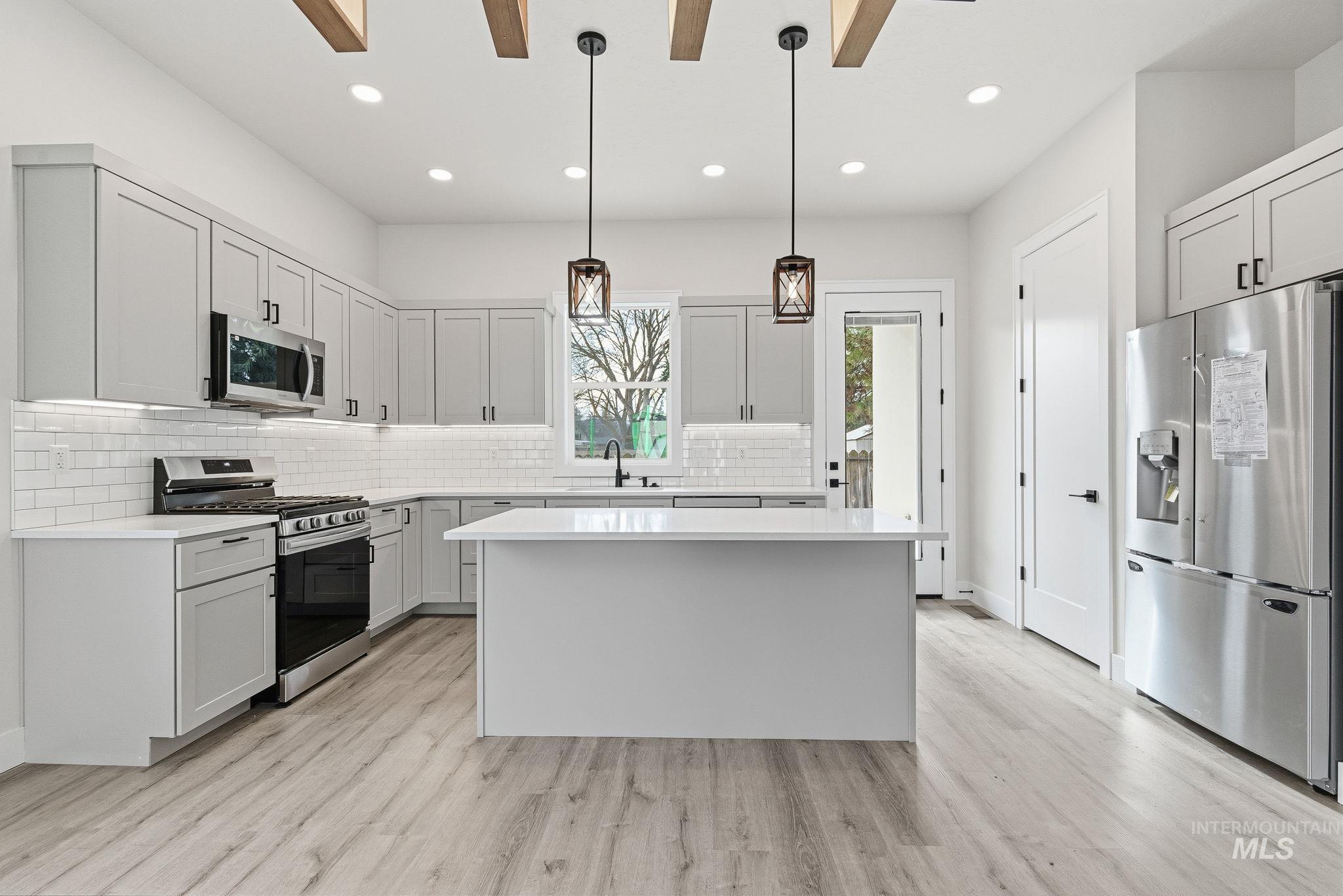6821 West Ustick Road Boise, ID 83704 - Photo 13 of 42 Kitchen with stainless steel appliances, a center island, decorative light fixtures, tasteful backsplash, and light wood-type flooring