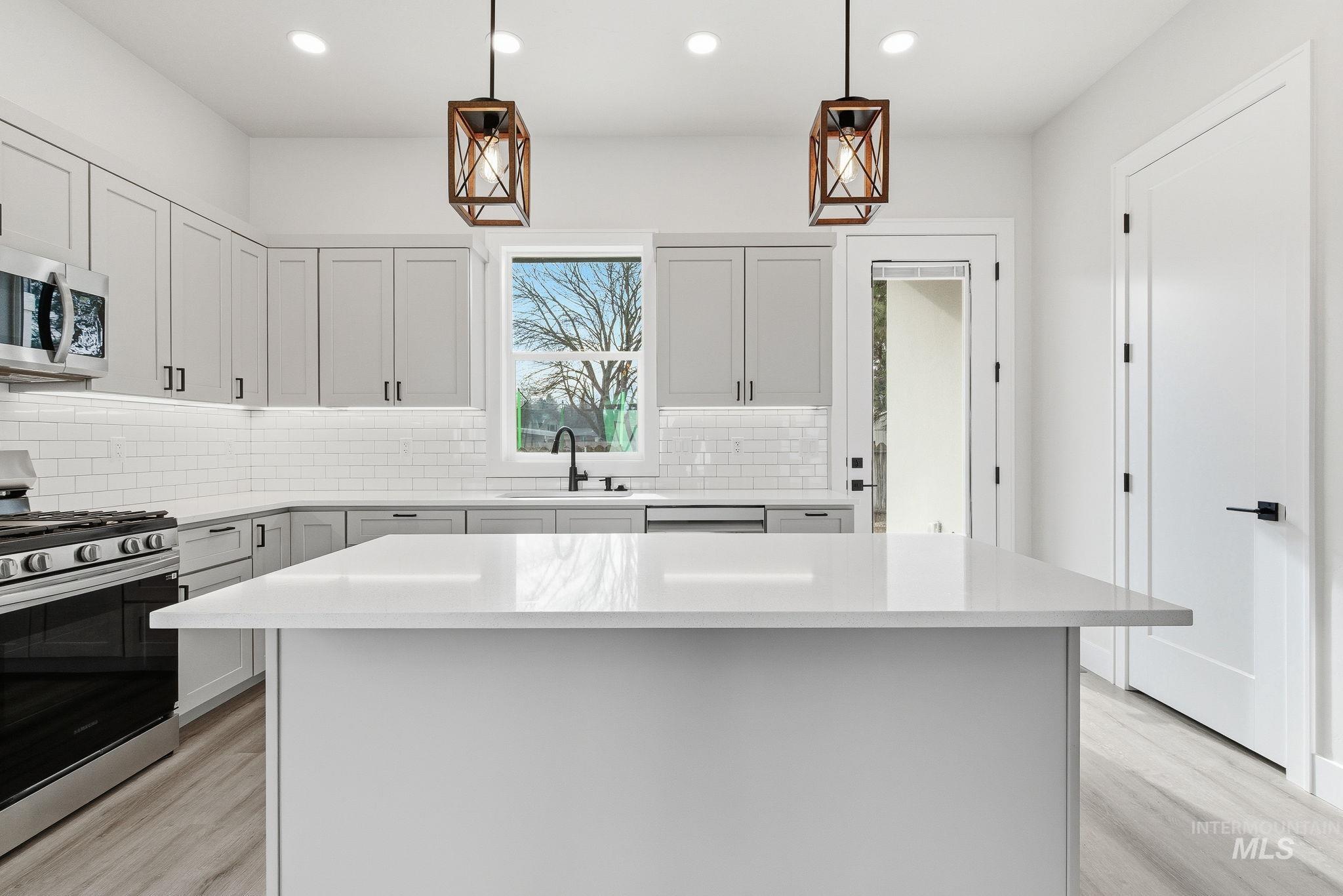 6821 West Ustick Road Boise, ID 83704 - Photo 14 of 42 Kitchen featuring stainless steel appliances, hanging light fixtures, a kitchen island, light stone countertops, and light wood finished floors