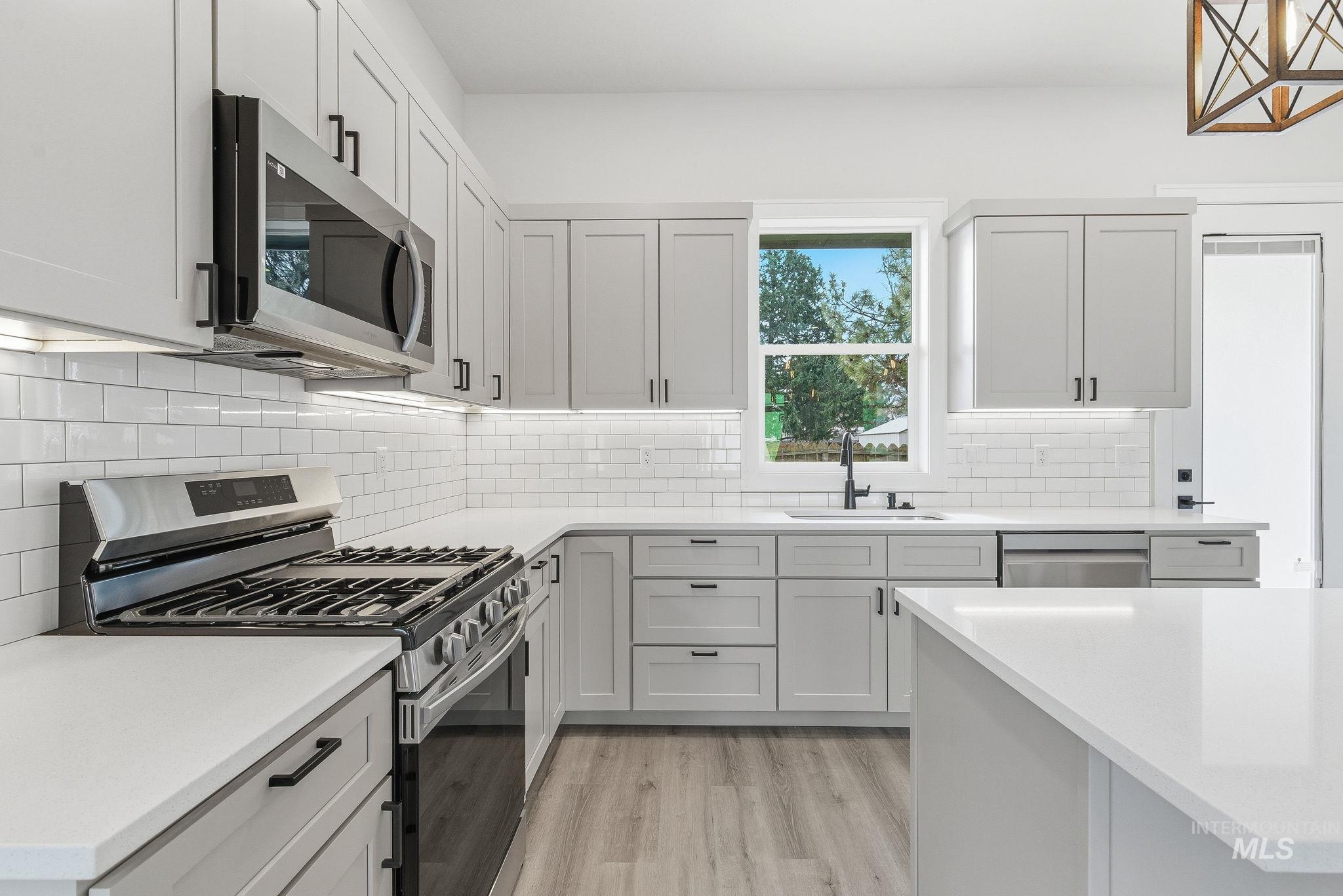 6821 West Ustick Road Boise, ID 83704 - Photo 15 of 42 Kitchen featuring stainless steel appliances, light wood-type flooring, light stone counters, white cabinetry, and decorative backsplash