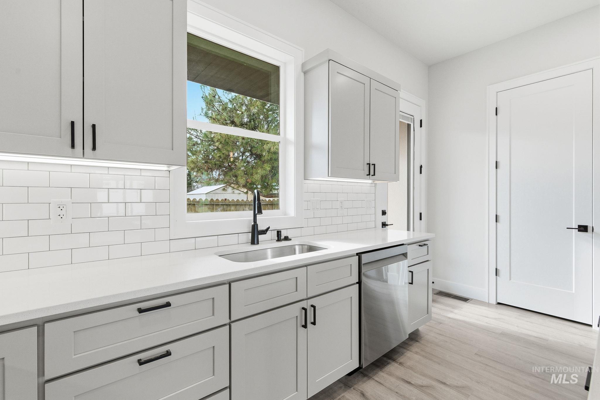 6821 West Ustick Road Boise, ID 83704 - Photo 16 of 42 Kitchen with dishwasher, white cabinets, light wood-style flooring, backsplash, and light stone countertops