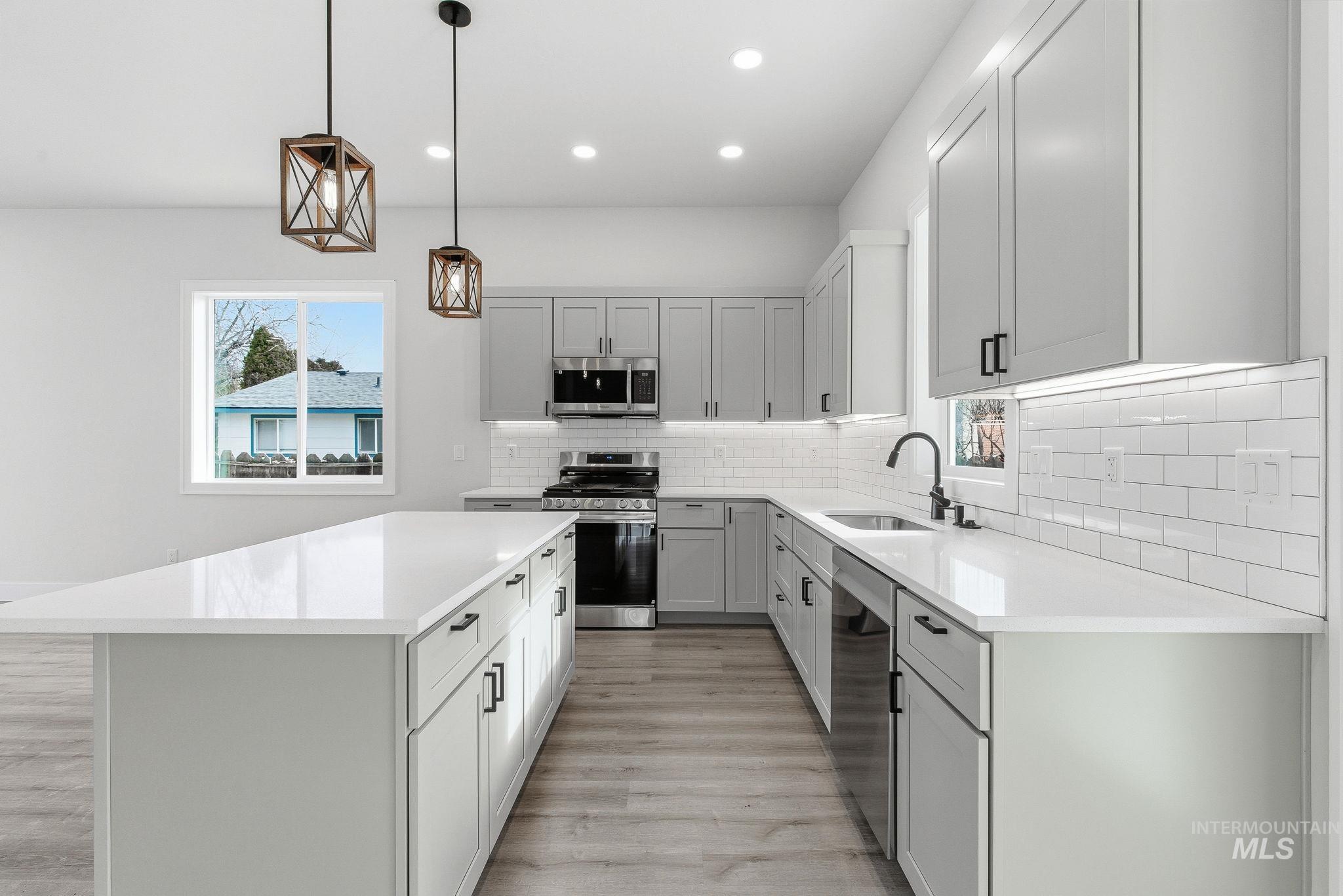 6821 West Ustick Road Boise, ID 83704 - Photo 18 of 42 Kitchen with decorative light fixtures, a kitchen island, stainless steel appliances, and light stone counters