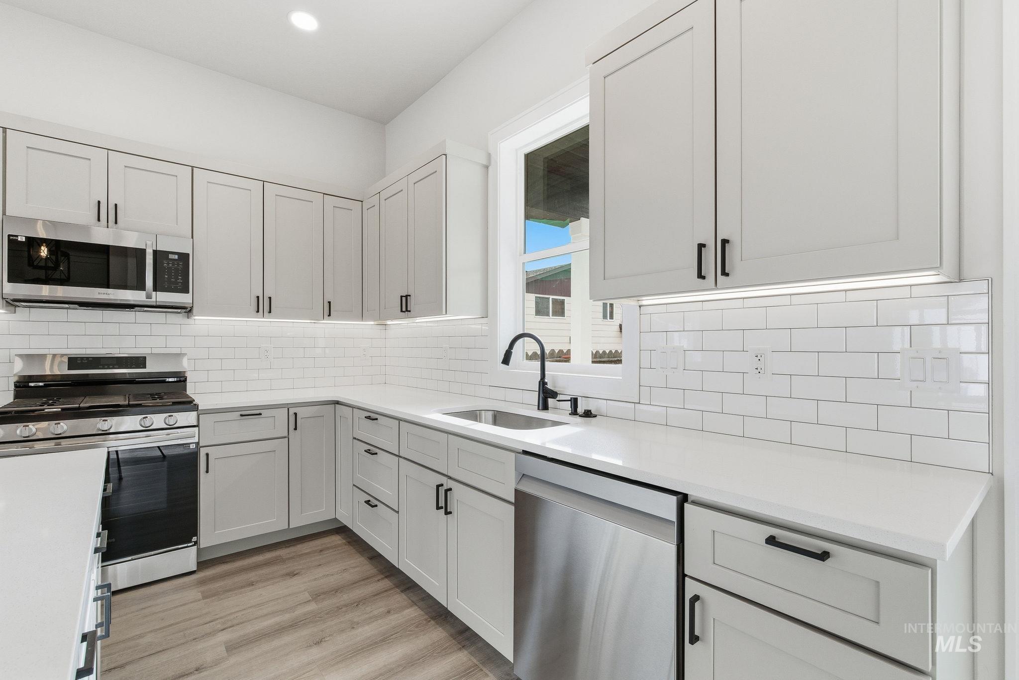 6821 West Ustick Road Boise, ID 83704 - Photo 19 of 42 Kitchen with stainless steel appliances, light wood-style floors, white cabinets, light stone counters, and tasteful backsplash