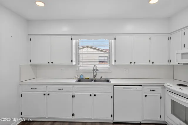 a kitchen with granite countertop white cabinets white appliances and a wide window