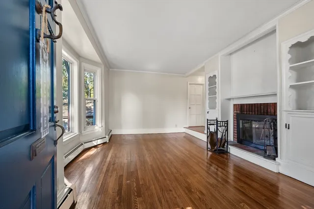 an empty room with wooden floor fireplace and windows