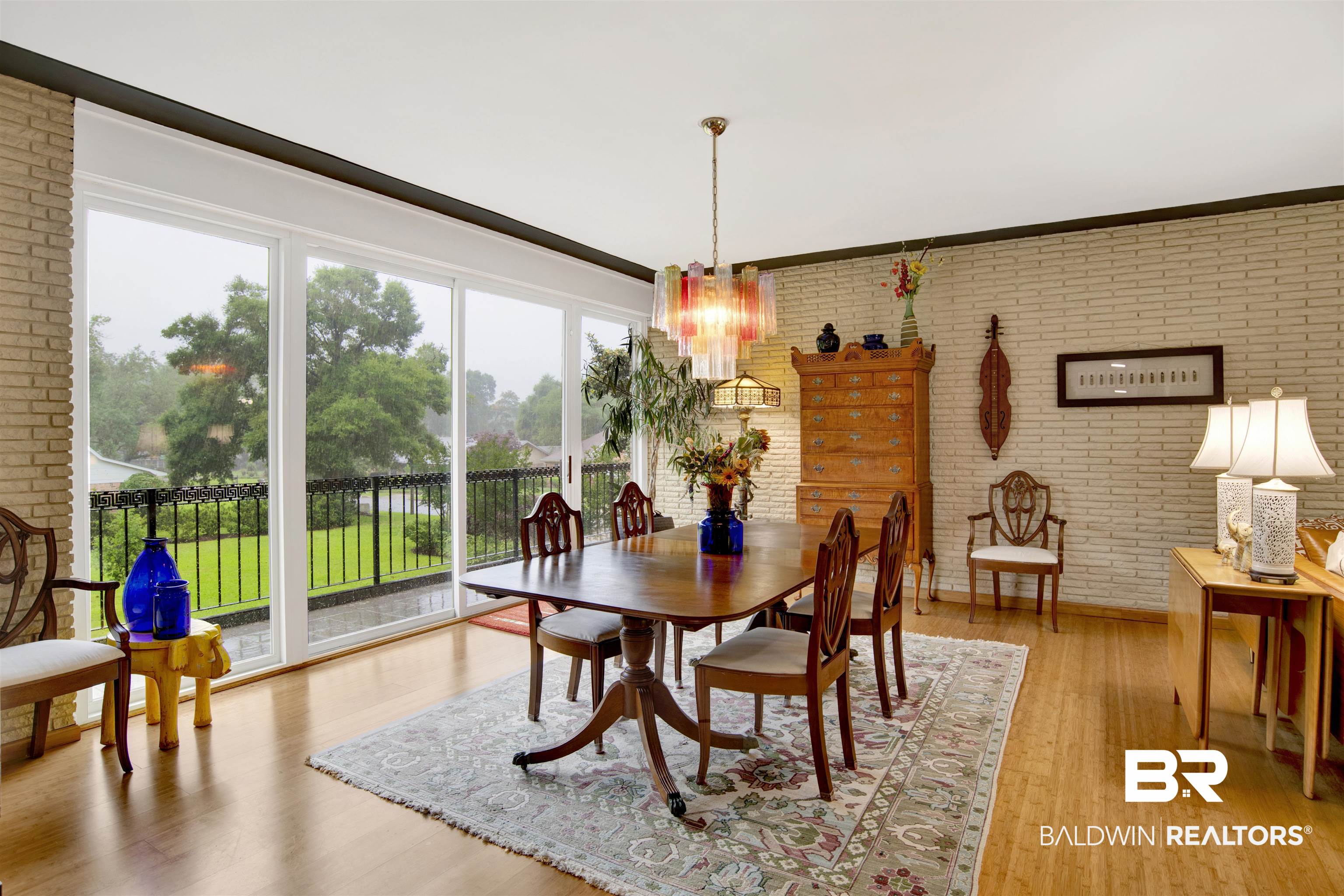 809 Bernard Circle Mobile, AL 36693 - Photo 25 of 75 Dining area featuring light brick walls, hardwood flooring, and a multi-pane sliding glass door opening to an outdoor balcony with a black wrought iron railing