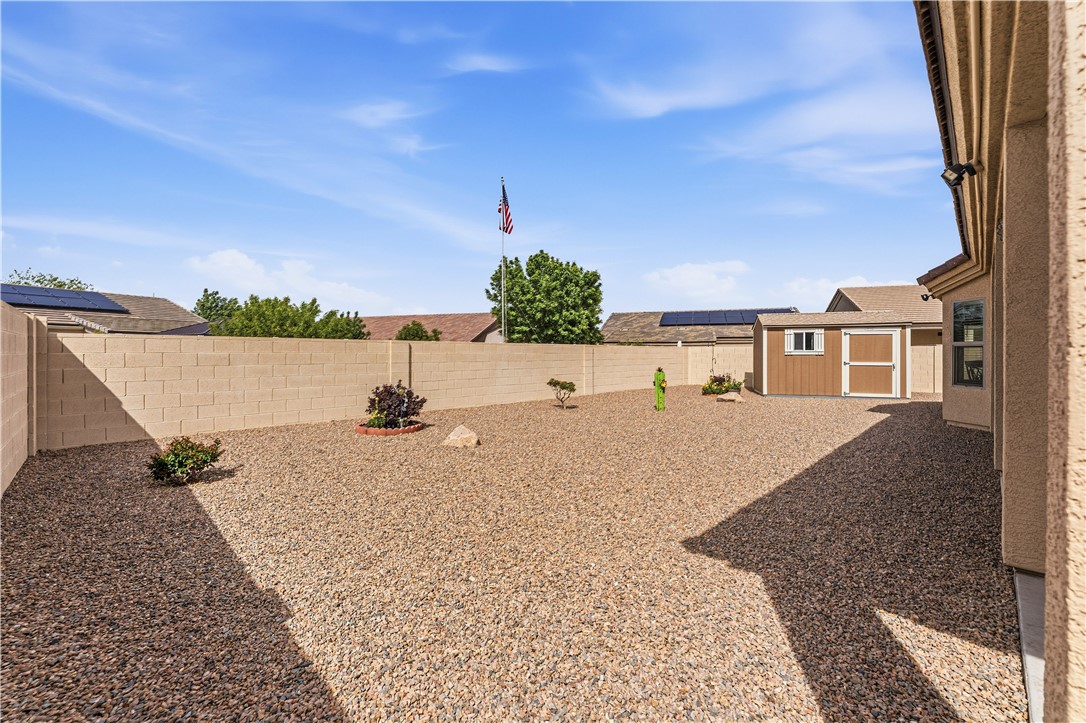 4143 North Stampede Road Kingman, AZ 86401 - Photo 40 of 42 Expansive rock-covered backyard featuring a block perimeter wall, a brown storage shed with white trim, and low-maintenance landscaping