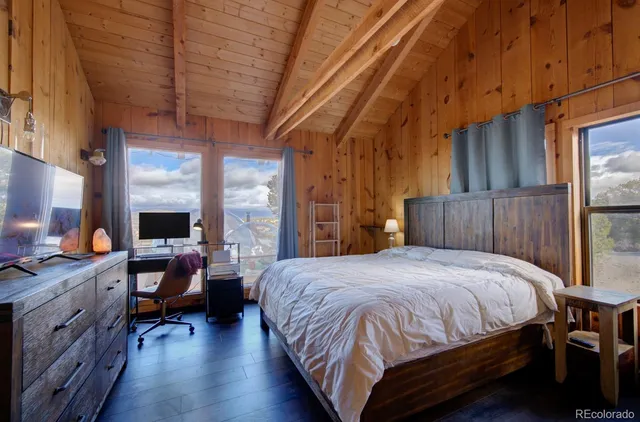 a bedroom with a bed a desk and chair with wooden floor