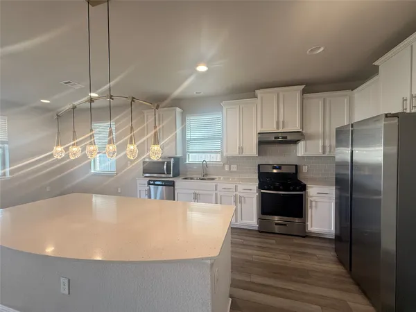 a large kitchen with stainless steel appliances a large counter top a stove a refrigerator and a sink