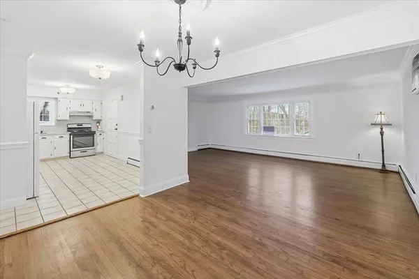 a view of an empty room with wooden floor and a kitchen