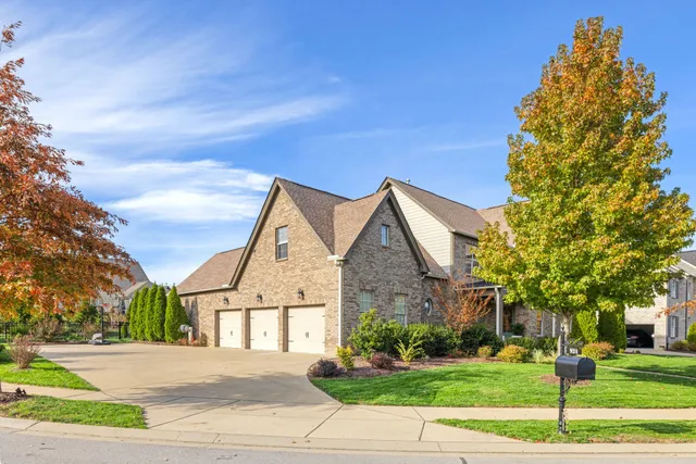 a view of a brick house next to a yard with large trees