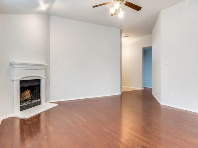a view of an empty room with wooden floor fireplace and a window