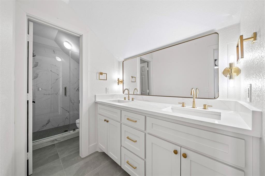 2104 Old McGarrah Road McKinney, TX 75072 - Photo 19 of 35 Dual vanity with integrated sinks, white cabinetry, gold-finish hardware, and a large rectangular mirror