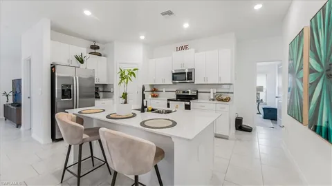 a kitchen with stainless steel appliances kitchen island granite countertop a dining table chairs and a refrigerator