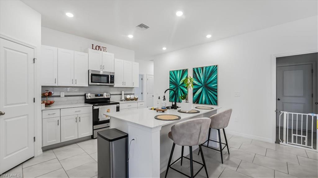 12252 Amber Waves Road Lehigh Acres, FL 33936 - Photo 10 of 35 a kitchen with stainless steel appliances kitchen island granite countertop a stove a sink a microwave and a refrigerator