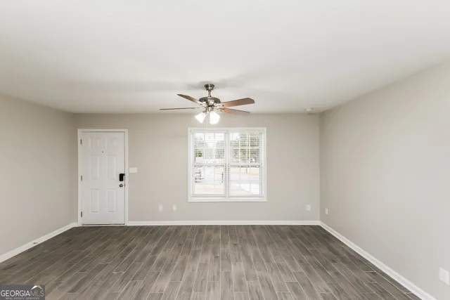 an empty room with wooden floor fan and windows