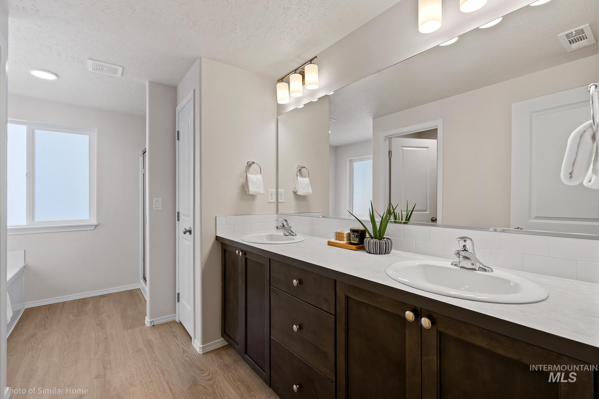 877 West Roan Ridge Nampa, ID 83686 - Photo 10 of 13 Bathroom featuring double vanity, light wood finished floors, a tub, plenty of natural light, and a textured ceiling
