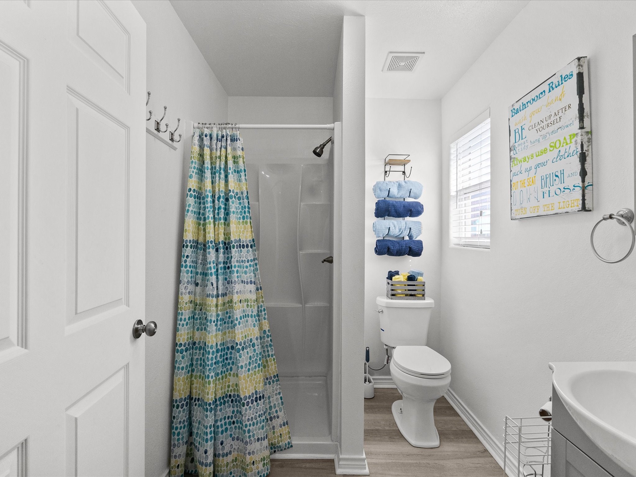 818 Surf Drive Surfside Beach, TX 77541 - Photo 16 of 29 This bathroom features a compact yet functional design with a shower and colorful curtain, a toilet with neatly organized towels above, and a small window for natural light. The space is bright and clean, with modern fixtures and a playful wall sign.