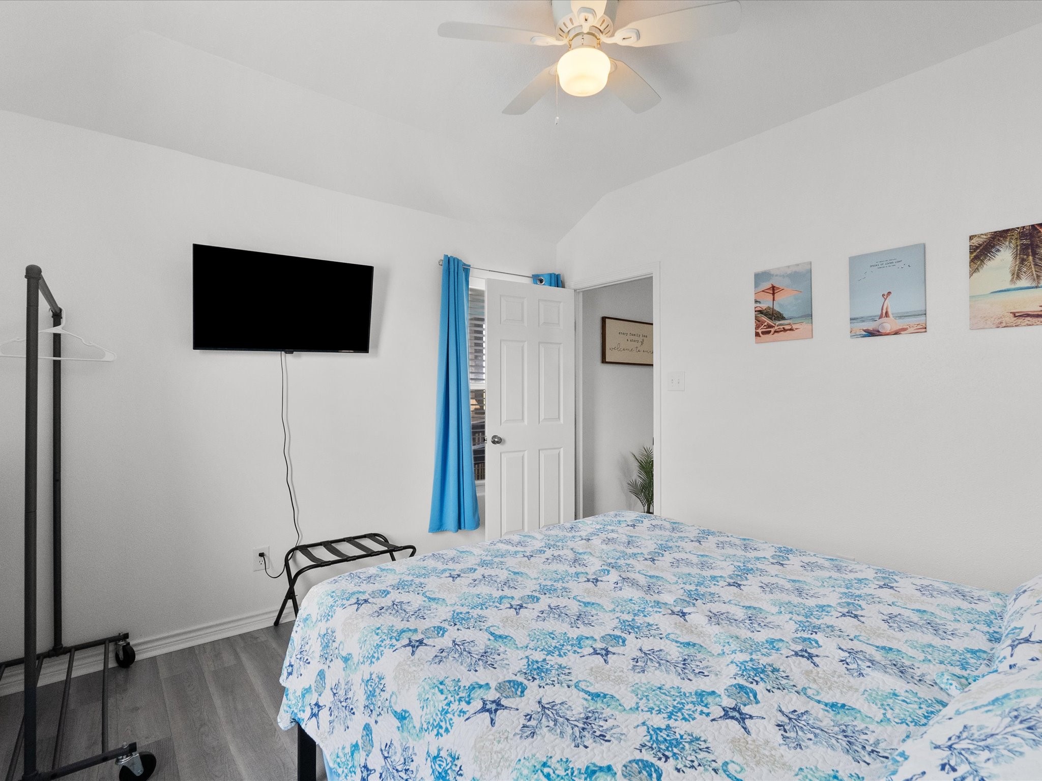 818 Surf Drive Surfside Beach, TX 77541 - Photo 19 of 29 This cozy bedroom features a ceiling fan, mounted TV, and vibrant blue decor. It includes a comfortable bed with a patterned quilt, open clothes rack, and wall art with a beach theme. Bright and inviting with modern flooring.