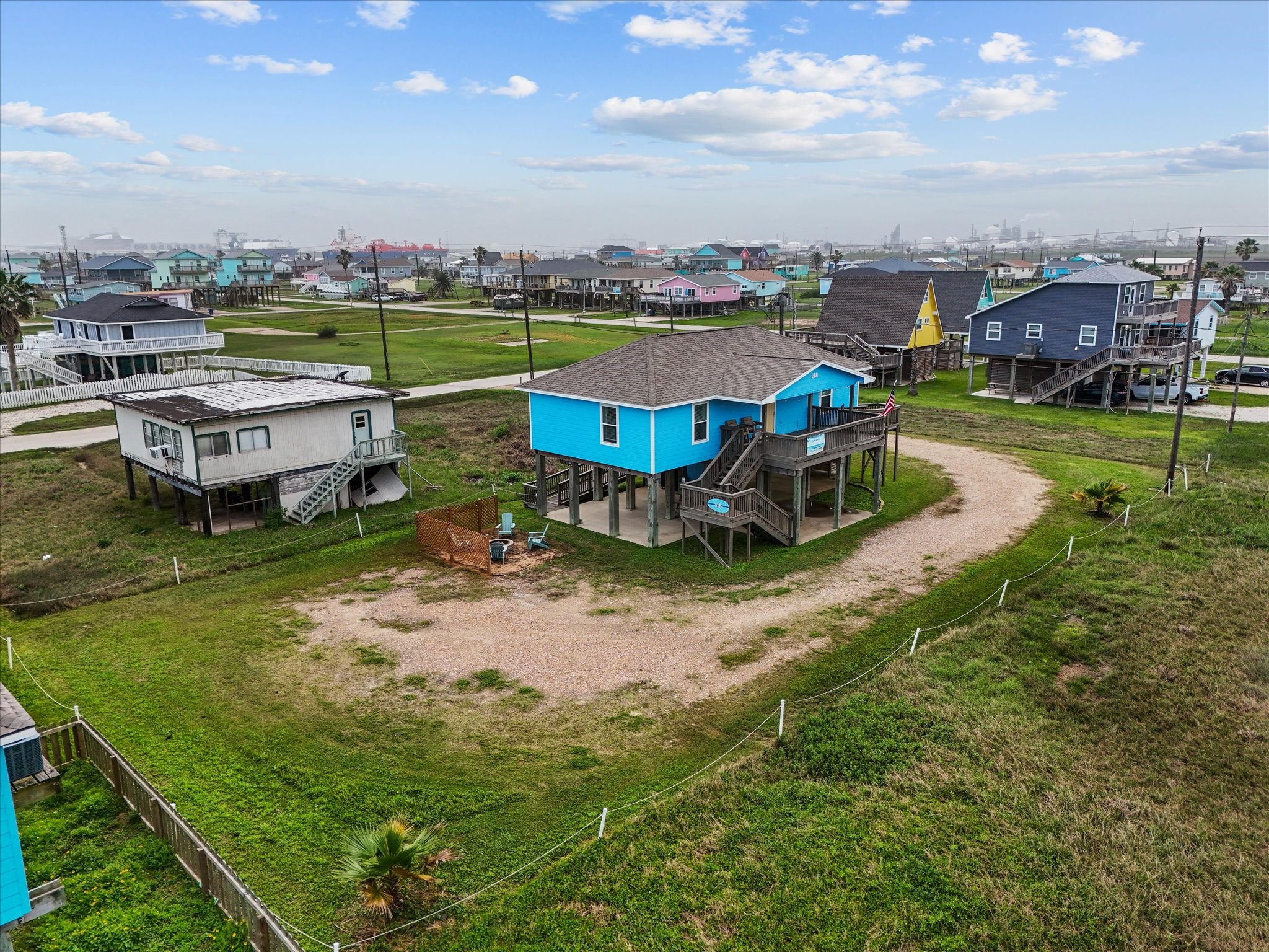 818 Surf Drive Surfside Beach, TX 77541 - Photo 2 of 29 This photo shows a vibrant blue beach house with a spacious yard and surrounding homes. The area is a coastal neighborhood with a mix of similar stilt houses, offering a relaxed, seaside lifestyle.