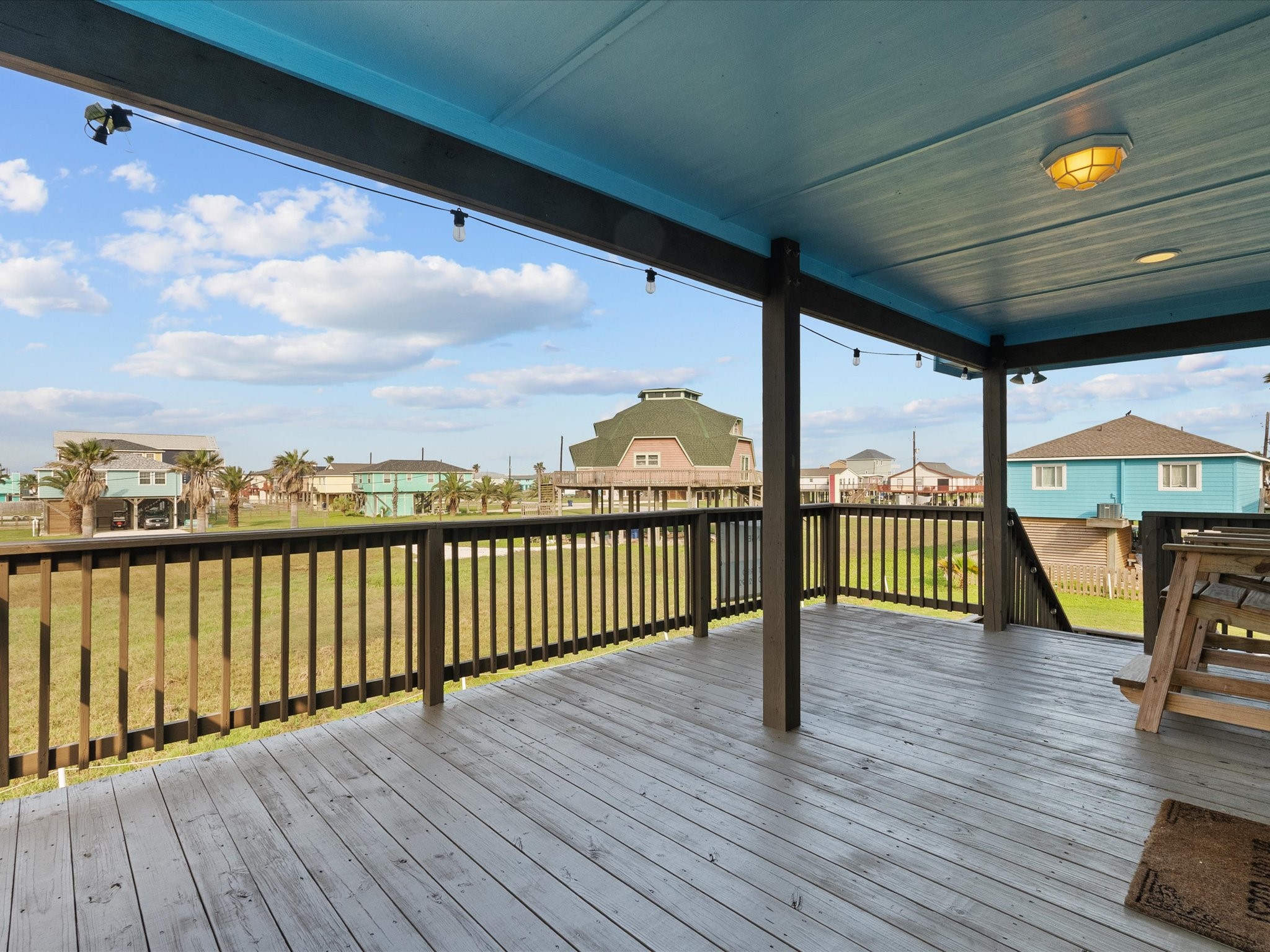 818 Surf Drive Surfside Beach, TX 77541 - Photo 24 of 29 This photo showcases a spacious, covered outdoor deck with a wooden floor, offering a scenic view of a neighborhood with palm trees and houses. Ideal for relaxing and enjoying the outdoors.