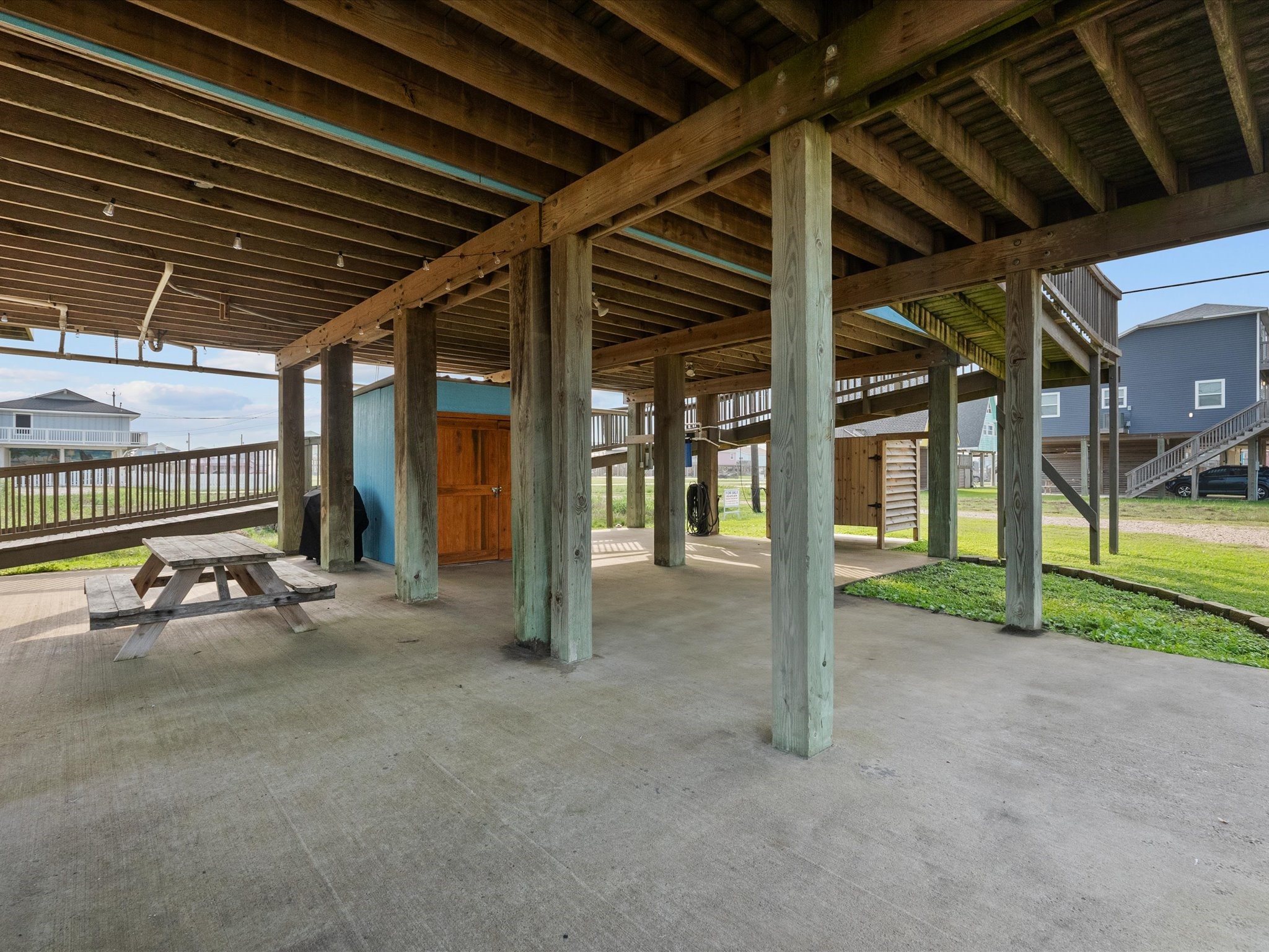 818 Surf Drive Surfside Beach, TX 77541 - Photo 25 of 29 This photo shows an open, covered area under a raised house with wooden support beams. It features a concrete floor, picnic table, and storage space, ideal for outdoor gatherings and parking.
