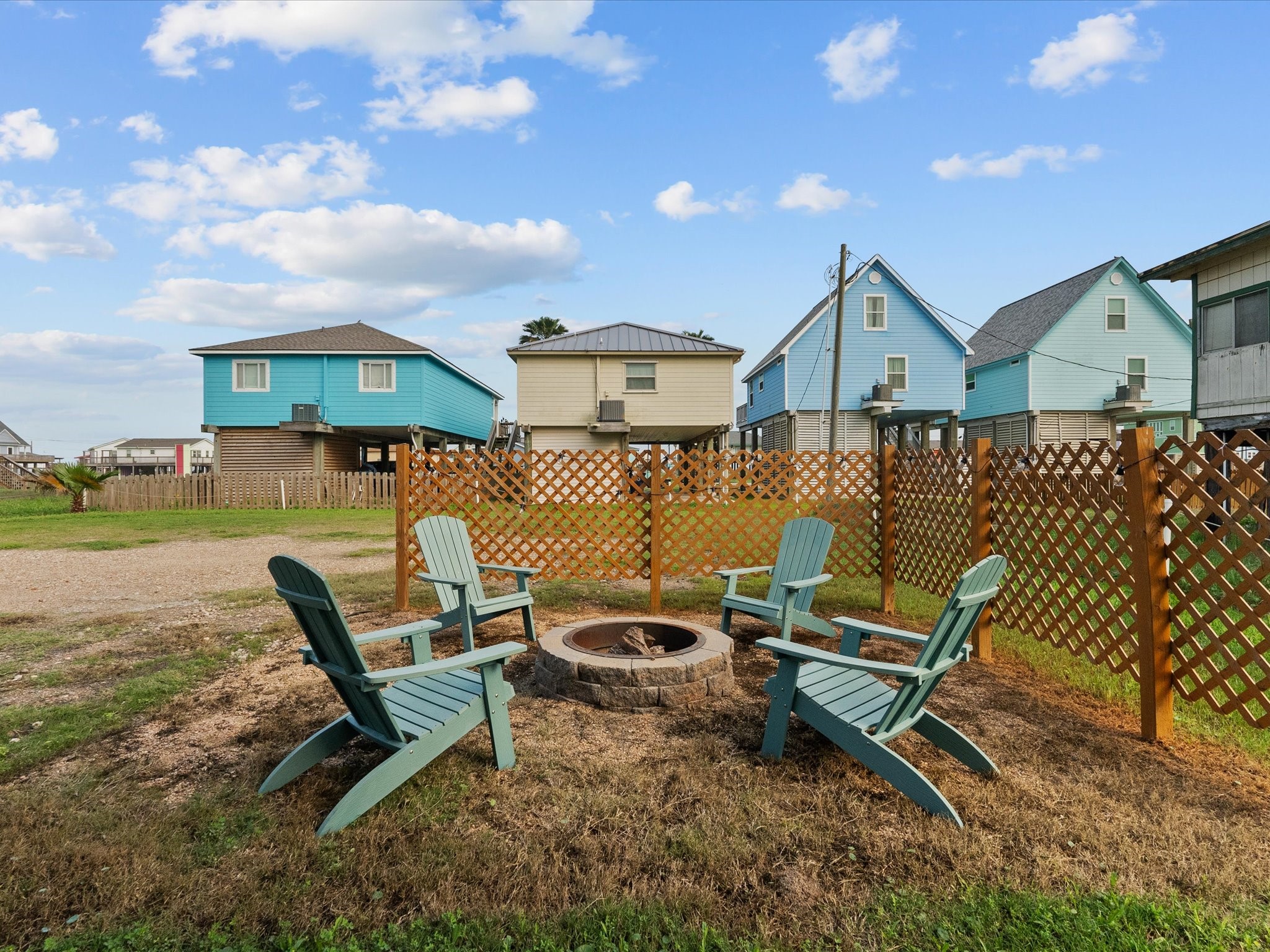 818 Surf Drive Surfside Beach, TX 77541 - Photo 27 of 29 Cozy outdoor area featuring a fire pit surrounded by four Adirondack chairs, enclosed by a wooden lattice fence. Perfect for relaxing and entertaining.