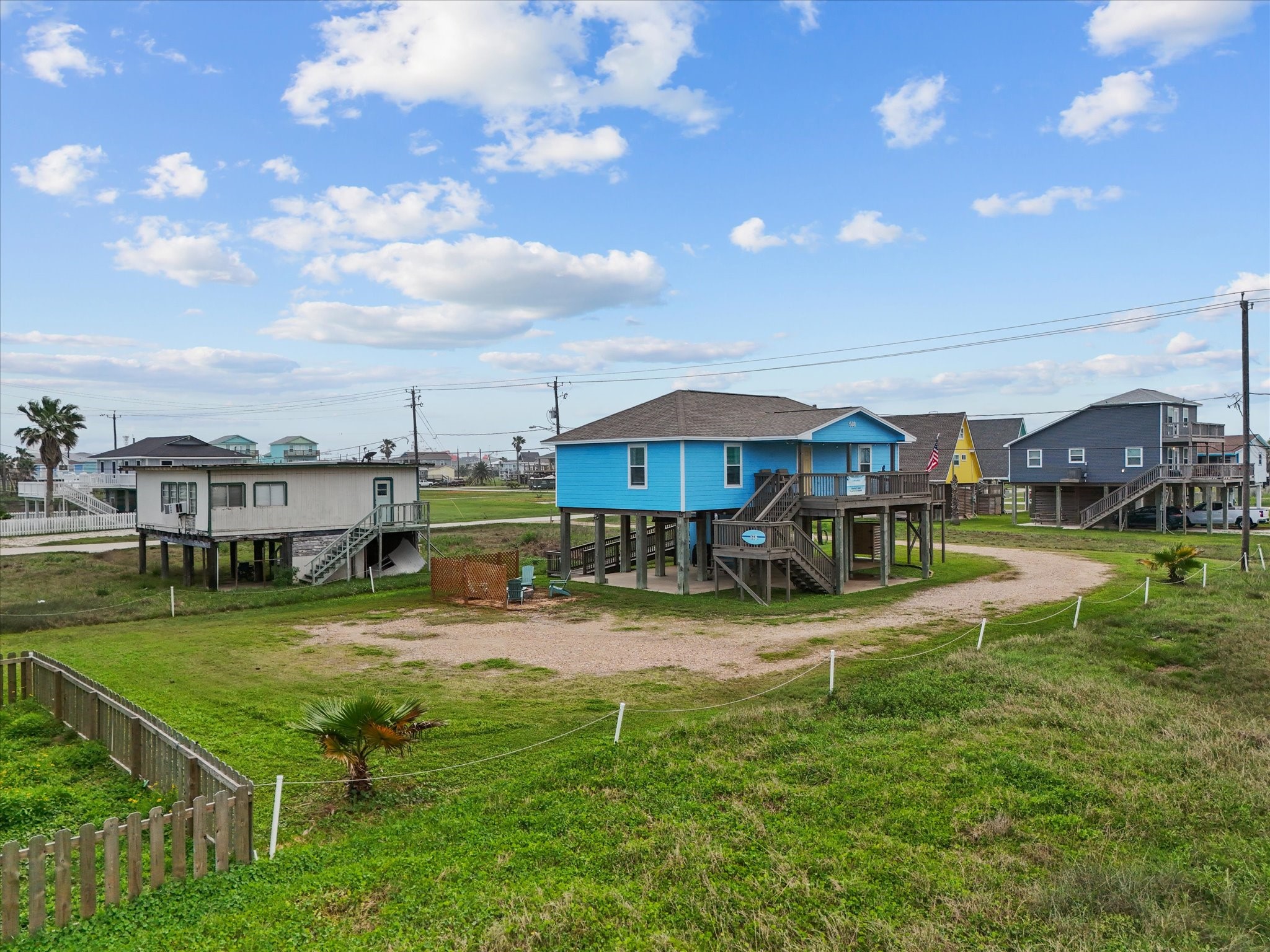 818 Surf Drive Surfside Beach, TX 77541 - Photo 7 of 29 This photo showcases a charming raised beach house with a bright blue exterior, set in a coastal neighborhood. The property features a spacious driveway, open green lawn, and is surrounded by similar elevated homes, offering a relaxed seaside atmosphere.