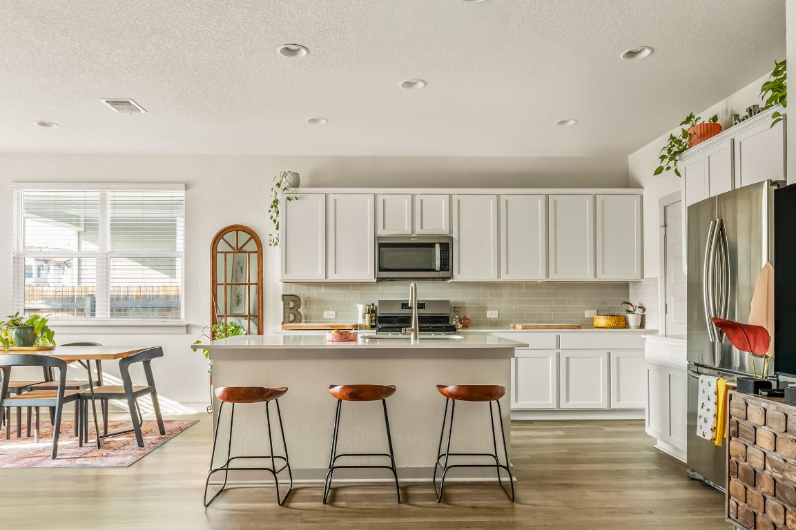 10002 Baden Lane Austin, TX 78754 - Photo 6 of 28 Kitchen with white cabinets, stainless steel appliances, a textured ceiling, light wood-style floors, and a breakfast bar