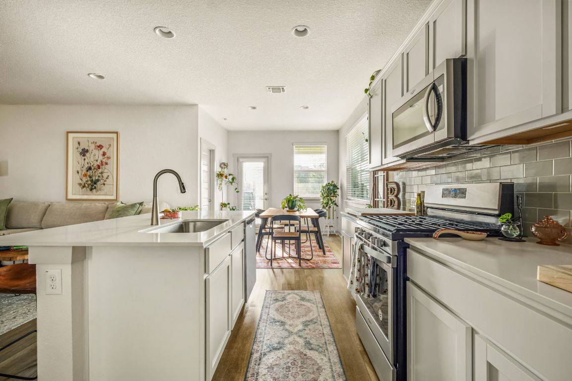 10002 Baden Lane Austin, TX 78754 - Photo 28 of 28 Kitchen with stainless steel appliances, a textured ceiling, open floor plan, dark wood-style flooring, and backsplash